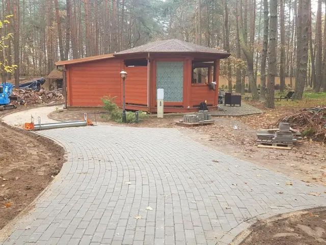 Ścieżka z kostki prowadząca do drewnianego pawilonu w lesie