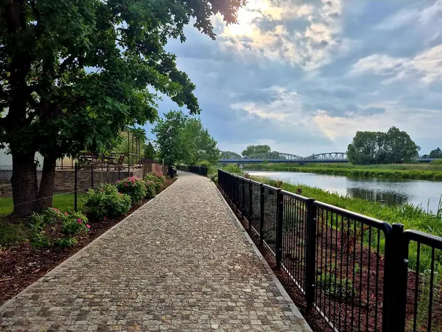Ścieżka z kostki wzdłuż rzeki, przy metalowej balustradzie