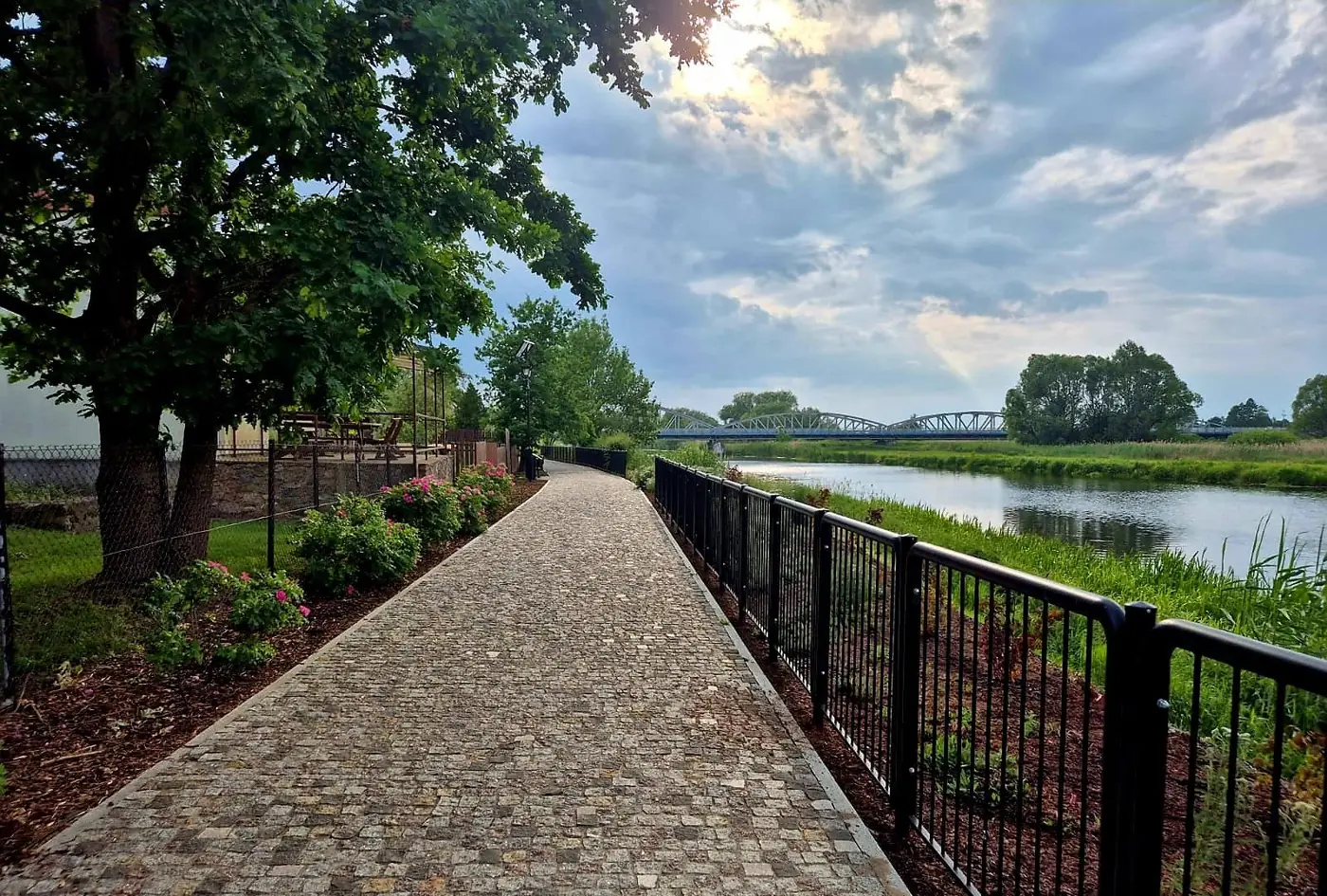 Ścieżka z kostki wzdłuż rzeki, przy metalowej balustradzie